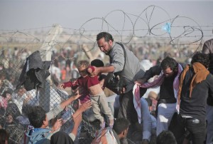 A Syrian refugee carries a baby over the broken border fence into Turkey after breaking the border fence and crossing from Syria in Akcakale, Sanliurfa province, southeastern Turkey, Sunday, June 14, 2015. The mass displacement of Syrians across the border into Turkey comes as Kurdish fighters and Islamic extremists clashed in nearby city of Tal Abyad. (AP Photo/Lefteris Pitarakis)